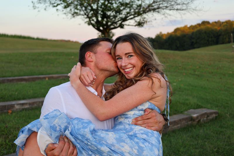 Engaged couple laughing in a field at golden hour